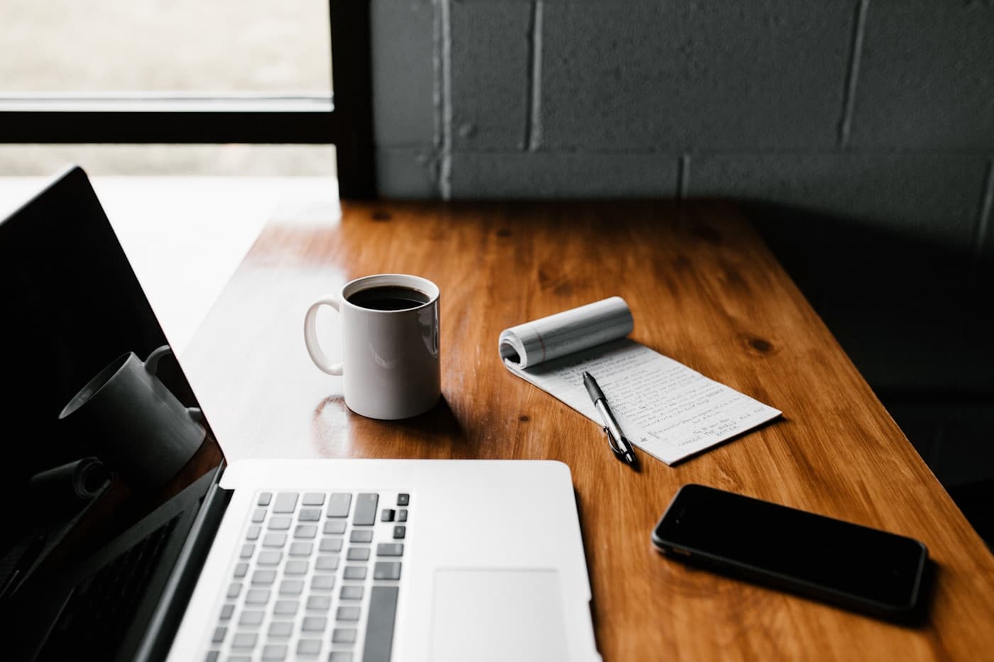 A laptop, smartphone, coffee and notepad on a wooden desk
